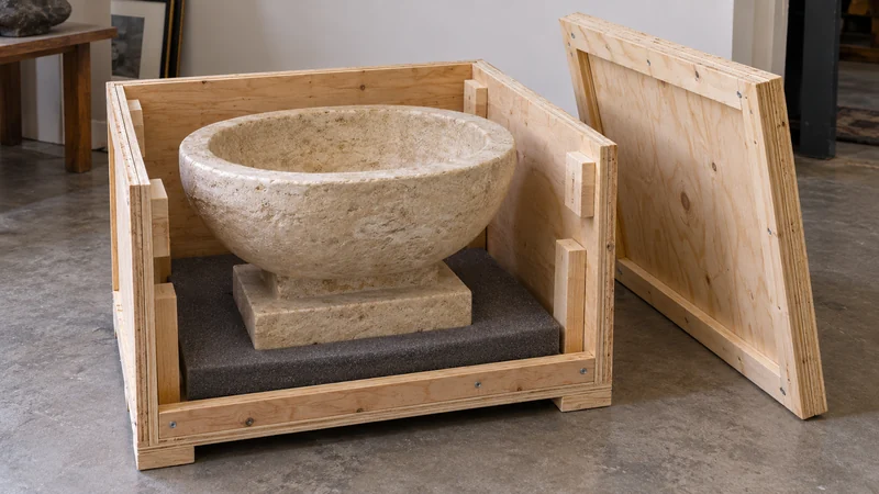 A small limestone vessel on a broad plinth sits in an open lined crate.
