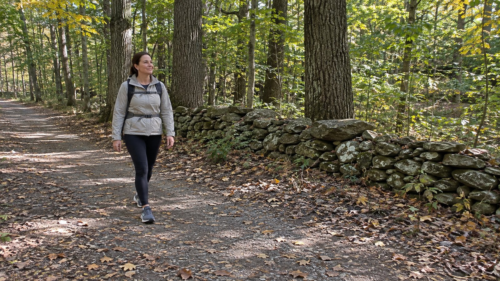 Test an outdoor routine A woman with a backpack walking a woodland path beside a low stone wall.