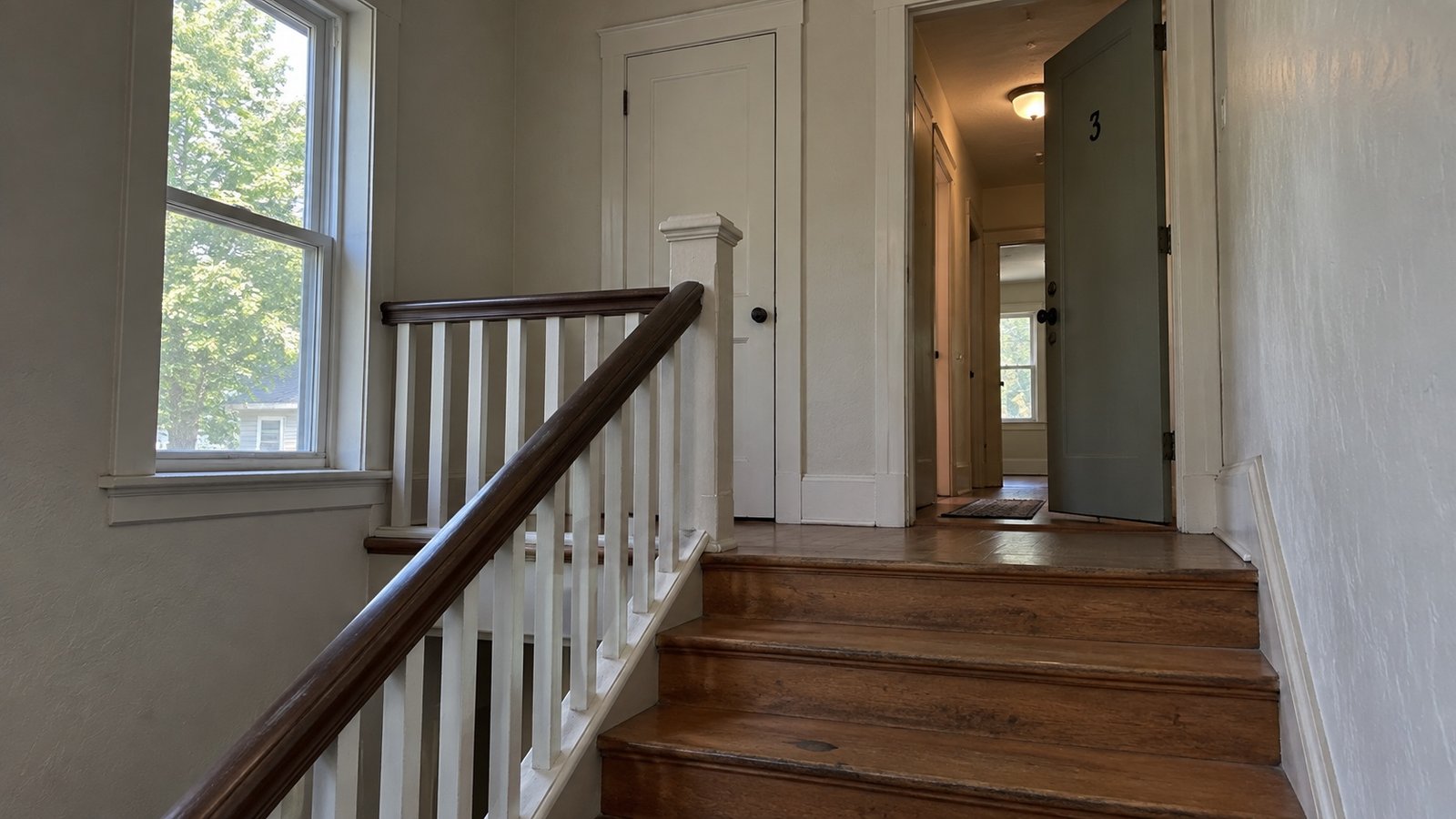 Wooden stairs rising to a landing and an open apartment doorway.