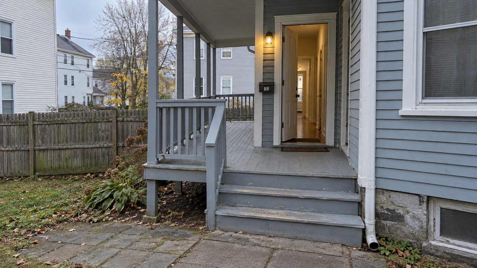Warm light beyond the side porch Side porch with three steps, a handrail and an open door from a paved residential yard.