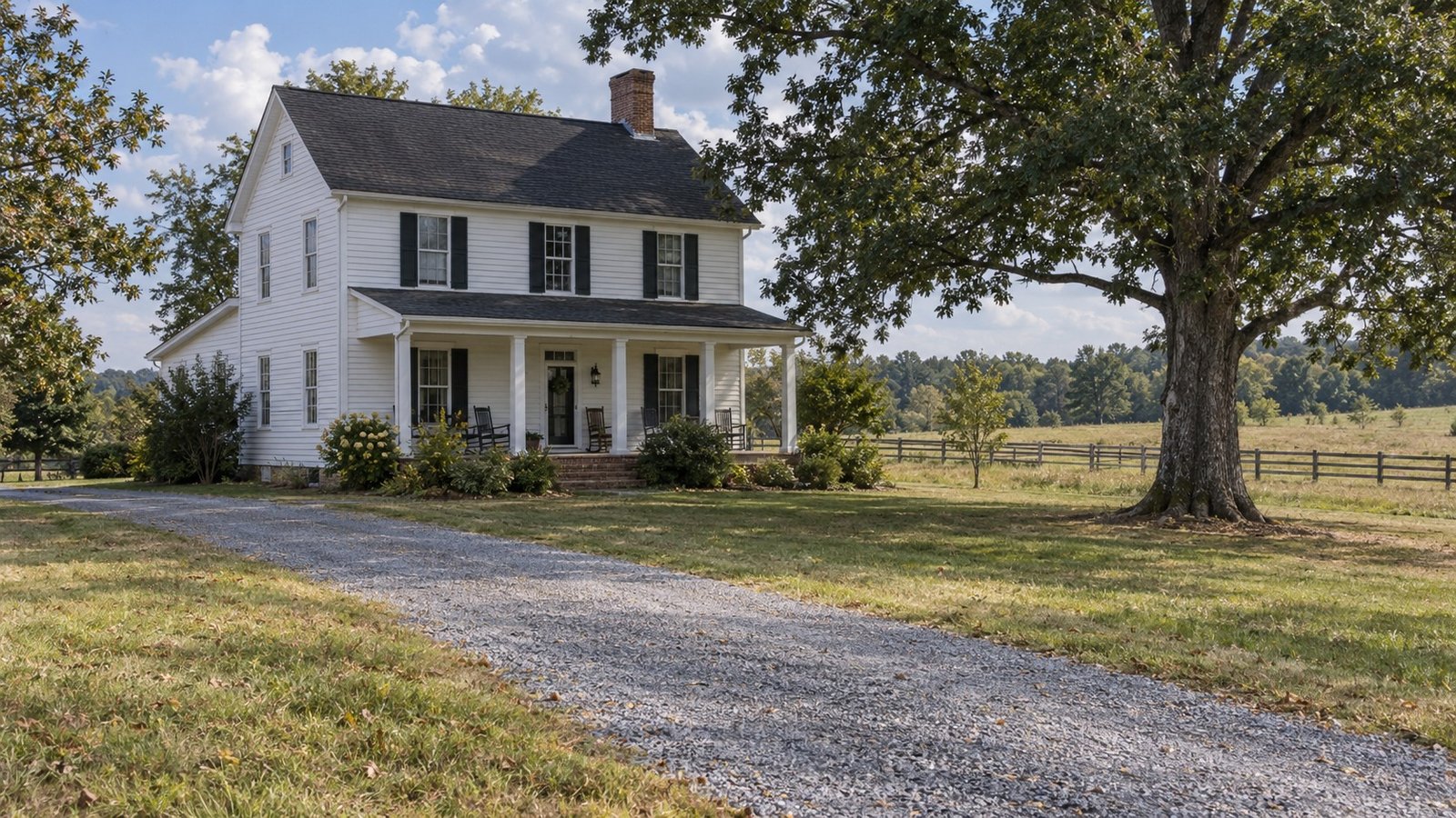 See the home and its approach A complete white rural farmhouse with a covered porch, gravel approach and mature trees.