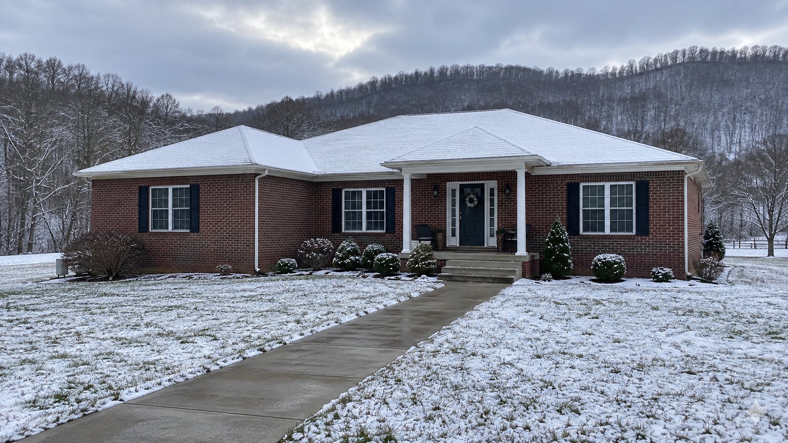 A whole brick house with a cleared walkway and light snow on the surrounding lawn