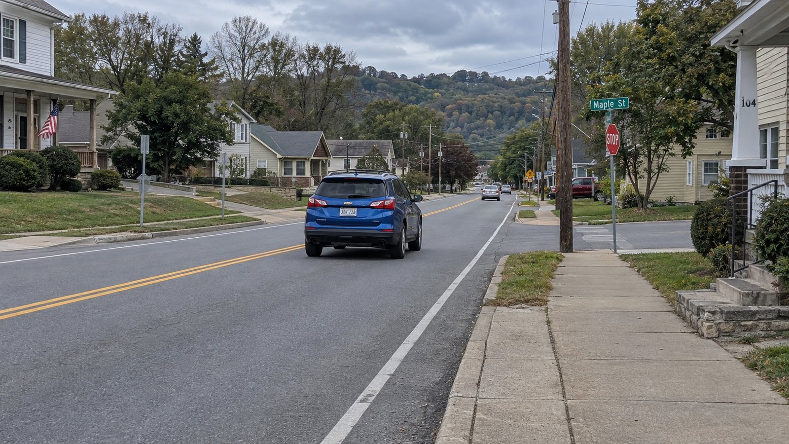 A whole blue SUV travels away in the right lane of a small-town road.