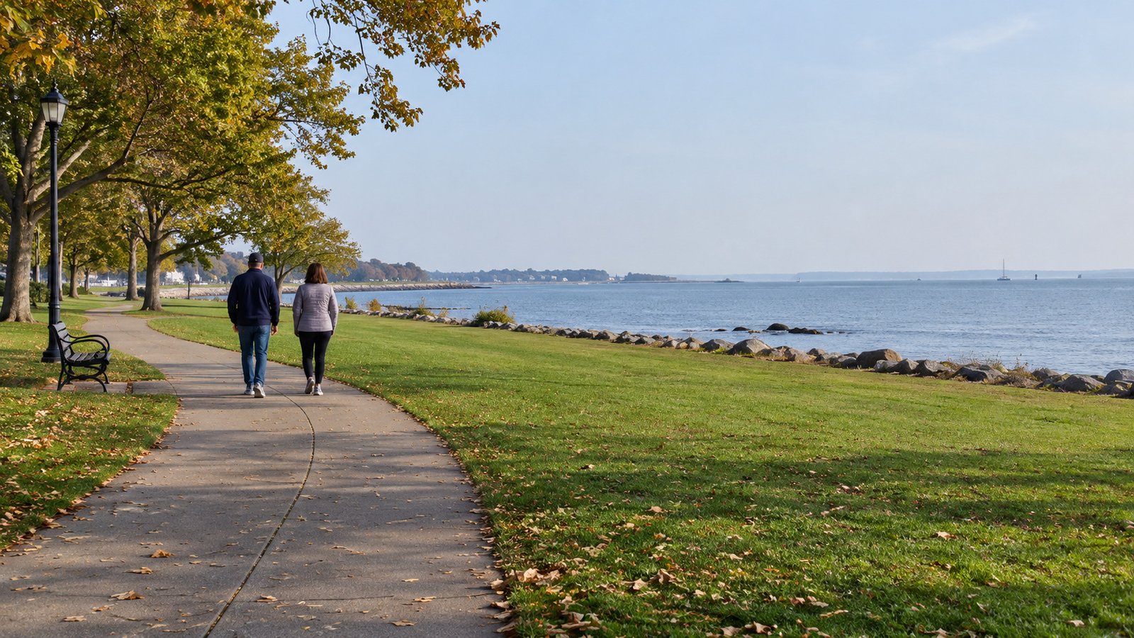 Two residents walking along a curving park path beside lawn and a low open-water shoreline.