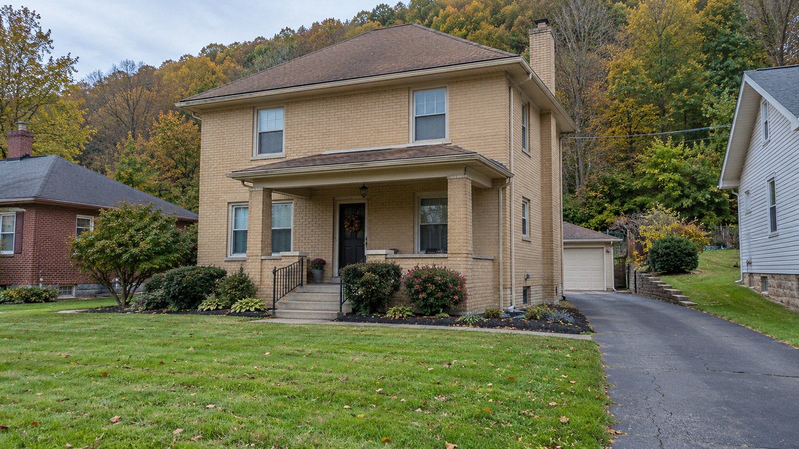 Plan the actual receiving home A complete two-story buff brick house with a covered front porch and paved side driveway below wooded hills.