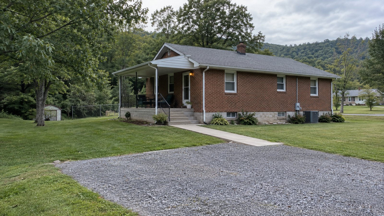 A complete single-story brick house with a covered porch, entrance steps, handrail and concrete walk leading to a gravel apron.