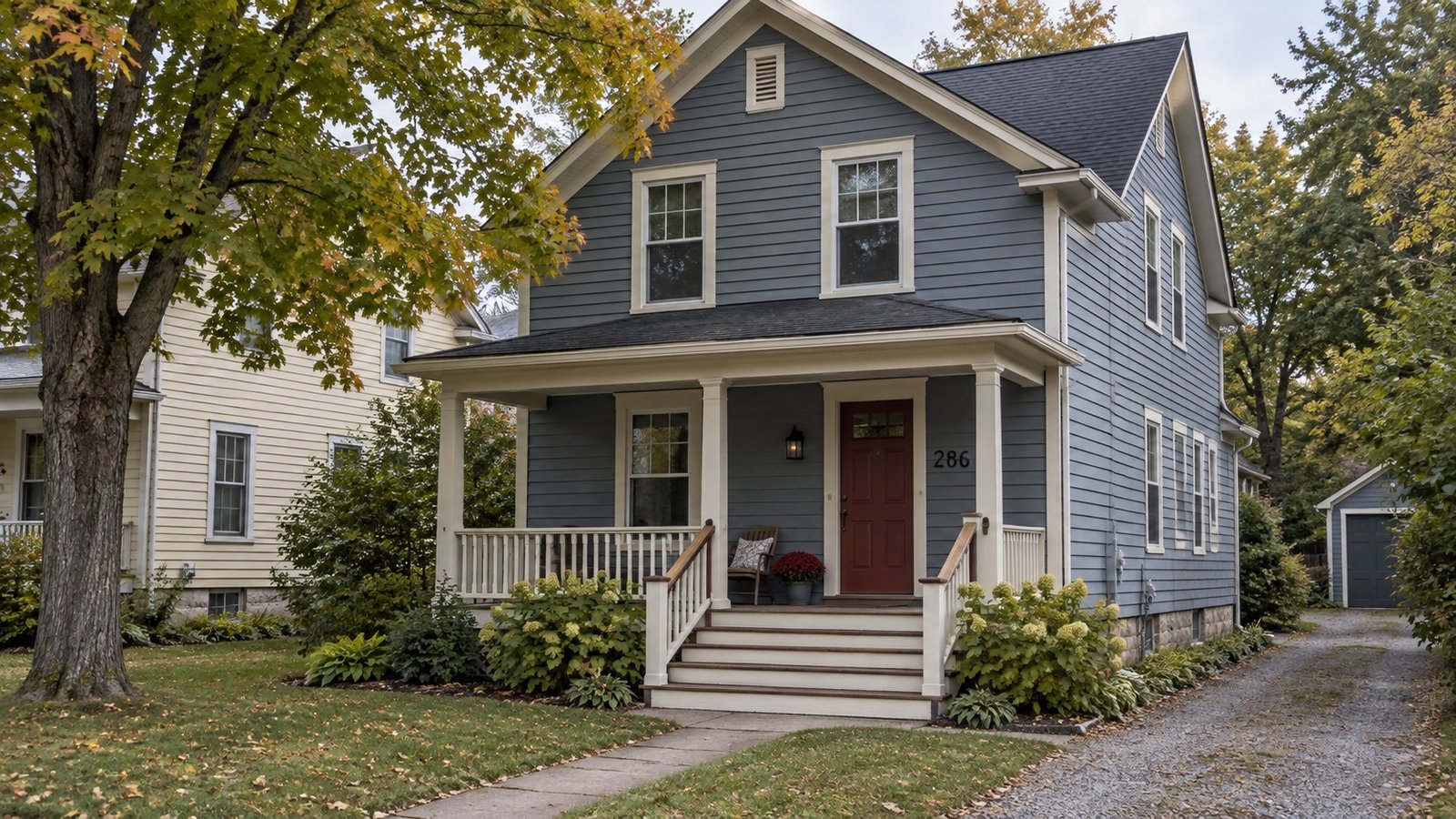 Blue-gray clapboard house with a covered porch, broad steps and a driveway beside the garden