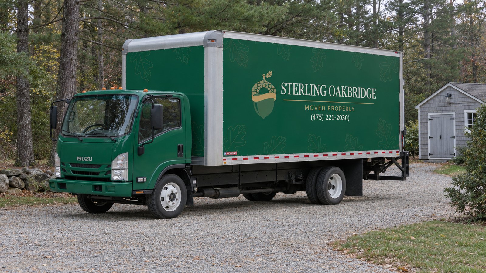 A complete green Sterling Oakbridge Isuzu NPR16 truck on a gravel driveway beside a shingle shed.