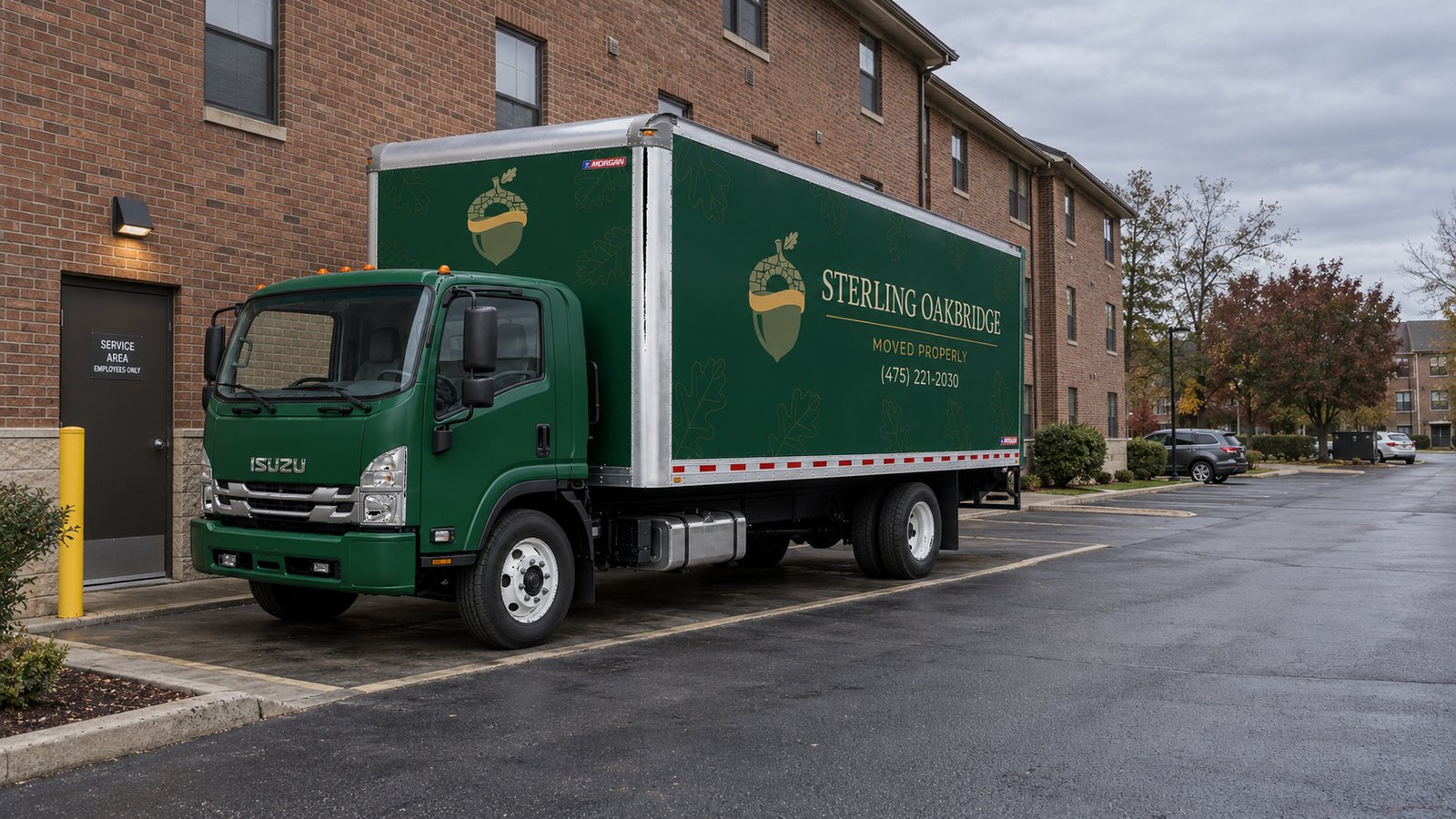 The complete vehicle footprint A green Sterling Oakbridge Isuzu FTR26 truck parked in a paved service bay beside a brick apartment building.