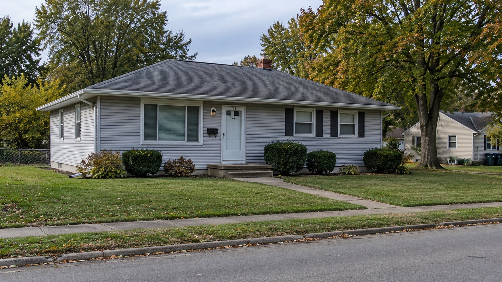 The house and its approach A pale gray ranch house with a shallow hipped roof, front steps, a paved walk and a small lawn.