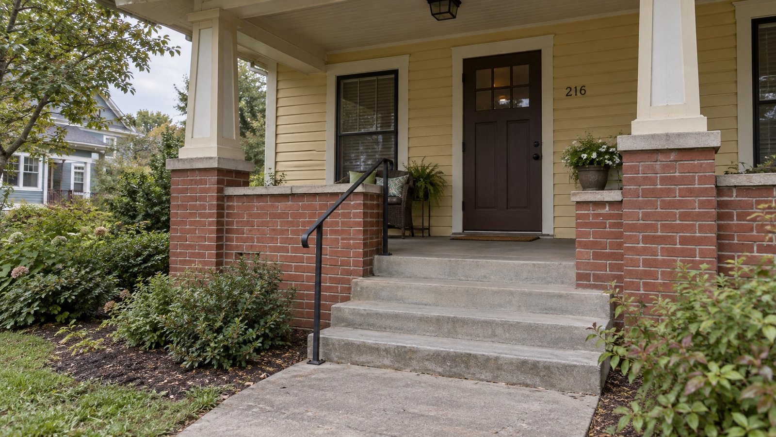 Broad front steps and continuous railing leading to a sheltered bungalow porch