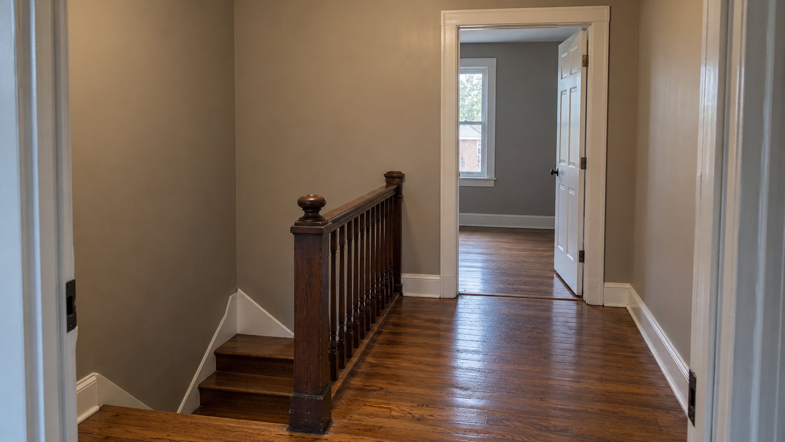 Review the stair landing and next doorway An upstairs timber stair landing with an attached balustrade and a complete open bedroom doorway beyond.
