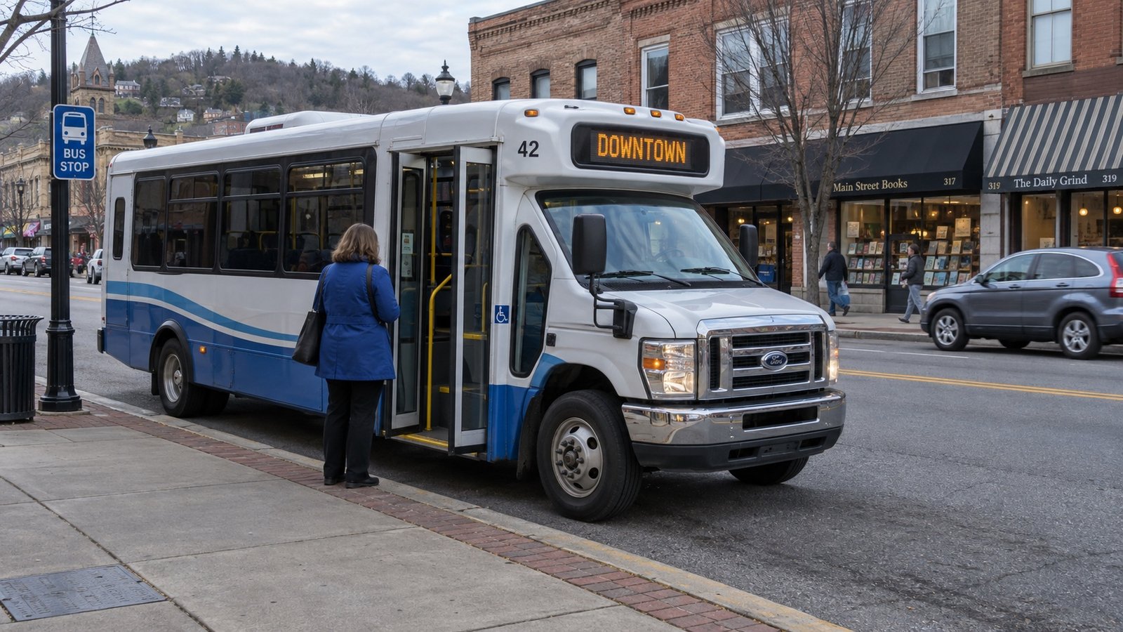 White and blue shuttle bus with a passenger waiting on the boarding sidewalk and a clear lane ahead