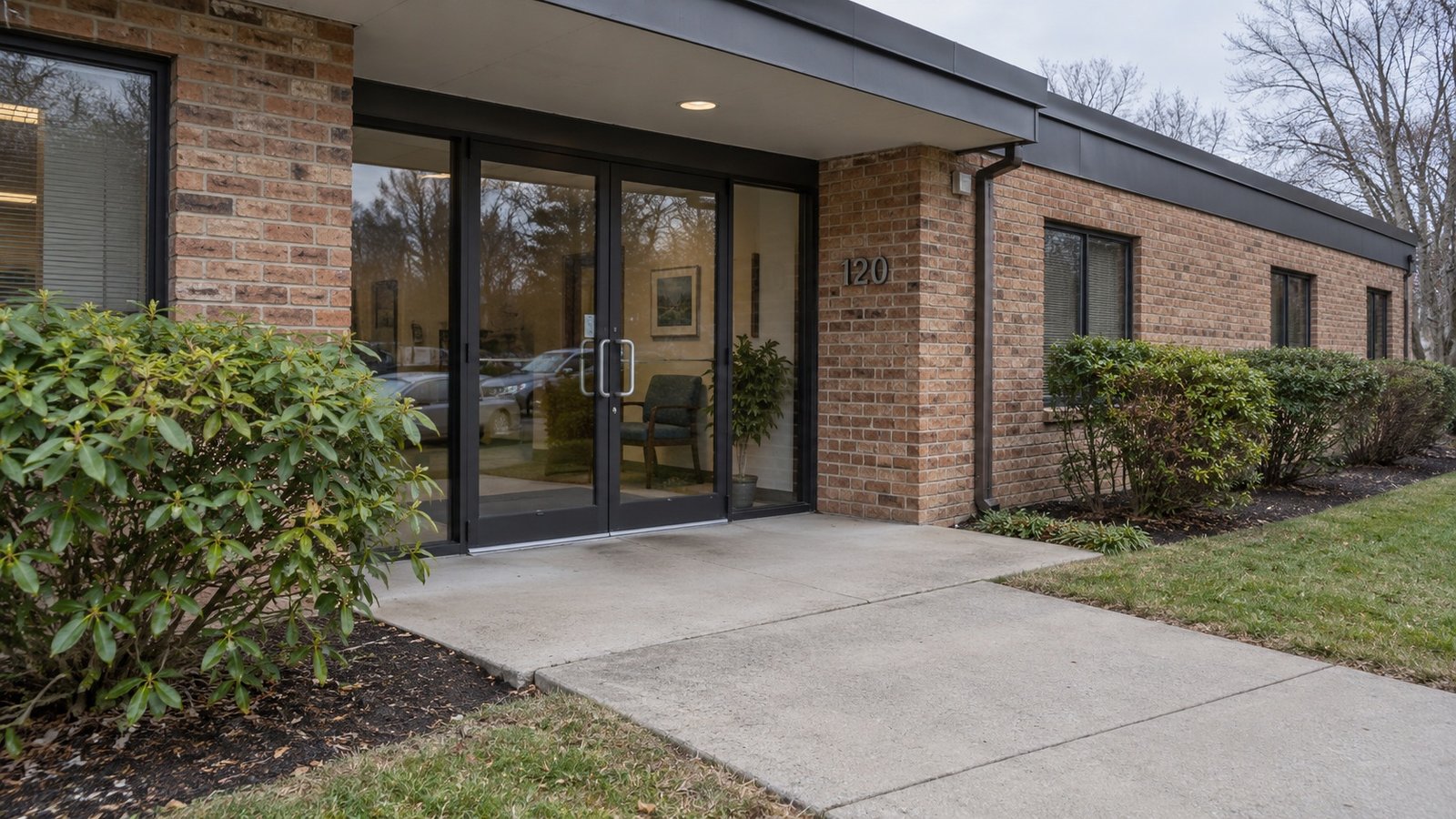 The office entrance Double glass doors beneath an overhang with a level concrete landing and clear paved approach