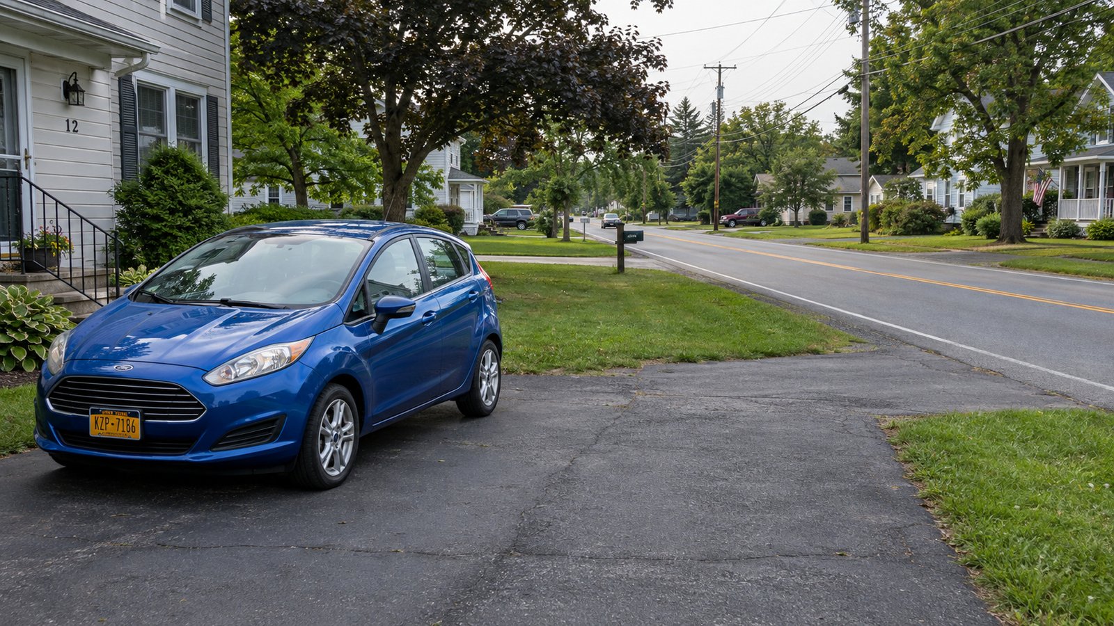 Starting a journey from home Blue compact hatchback parked on a paved residential driveway beside a clear two-lane road