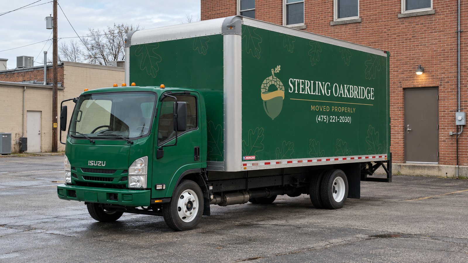 A truck at a business entrance Dark green Sterling Oakbridge Isuzu box truck on pavement beside the rear door of a brick commercial building