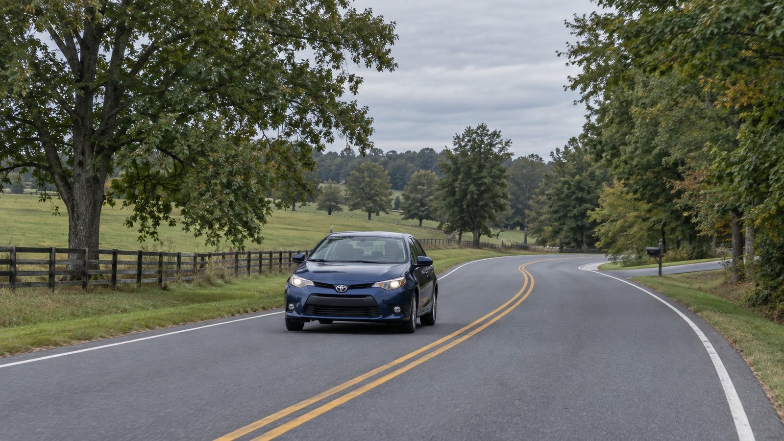 Try the complete everyday journey A complete blue sedan approaching on a rural two-lane road with oaks and a pasture fence.