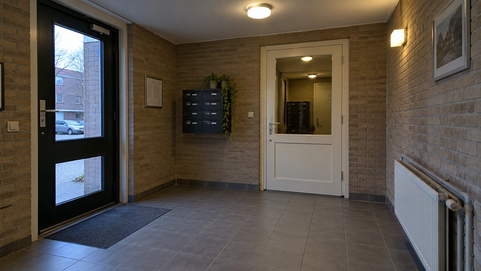 Check the entrance and door swing Brick entry vestibule with two closed glazed doors, a tiled floor and mailboxes