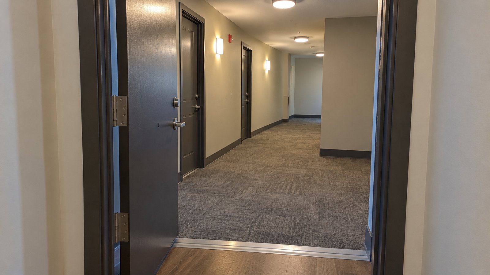 The corridor after the apartment threshold An open apartment entrance looking over a level threshold into a clear carpeted common corridor and its right-hand turn.