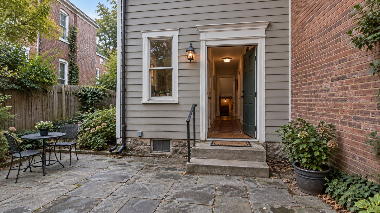 The complete rear-entry route An open wooden rear door, complete two-step landing and rail, paved courtyard and a hallway leading toward cellar stairs.