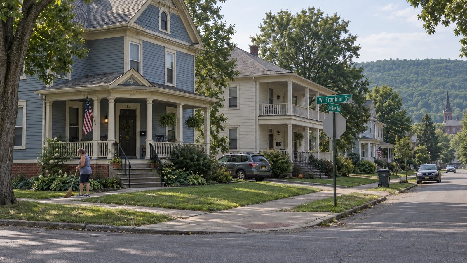 A residential street of older frame houses with porches and parked cars.