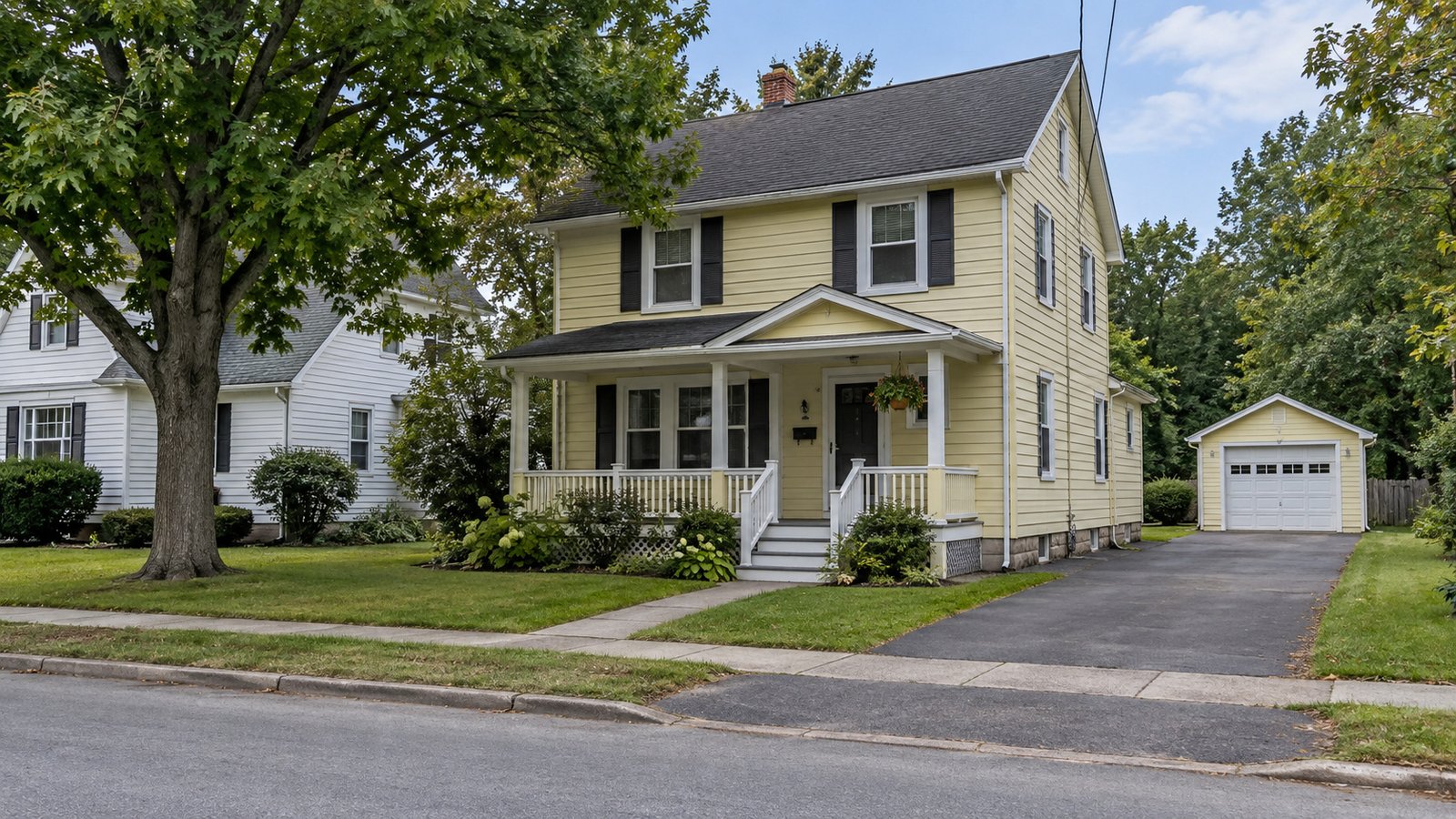 House, porch and garage approach Pale yellow two-story house with a covered porch, front steps and a paved driveway leading to a detached garage