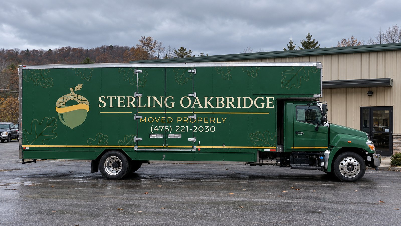 Space for the moving vehicle Dark green Sterling Oakbridge Hino box truck in side profile on a private commercial forecourt