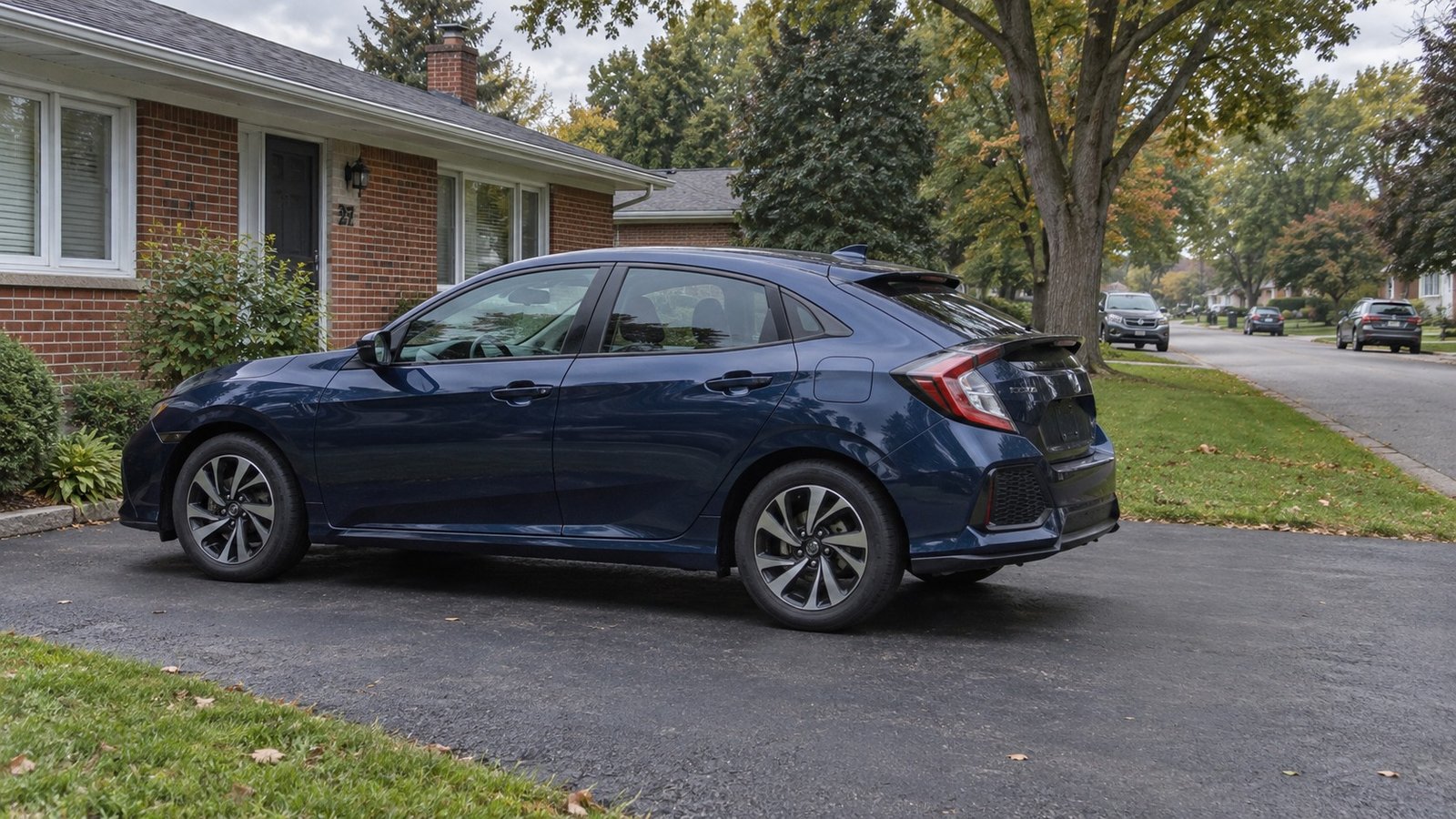 A complete ordinary car on a private asphalt drive beside a brick house.