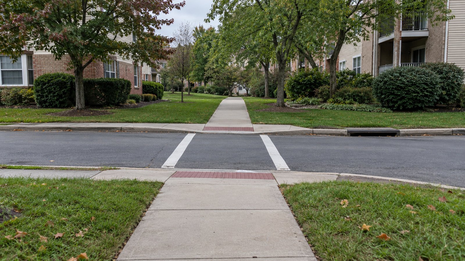 Follow both sides of the crossing A painted crossing links two aligned curb ramps and continuous sidewalks between brick-and-siding homes.