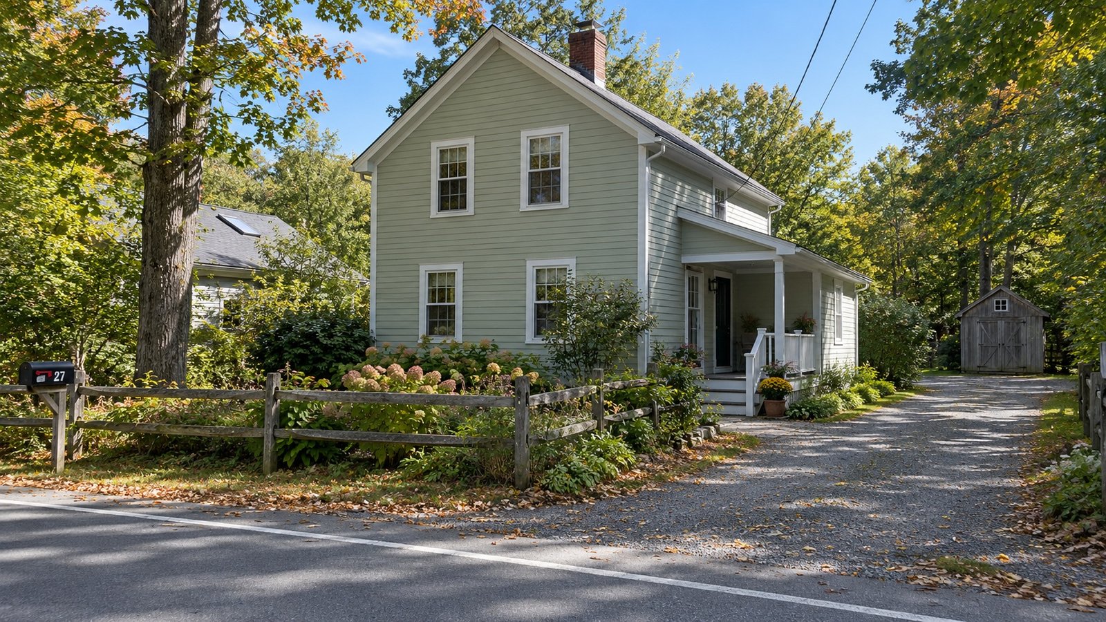 Pale green two-story clapboard house with a side porch, timber fence and gravel driveway leading to a shed