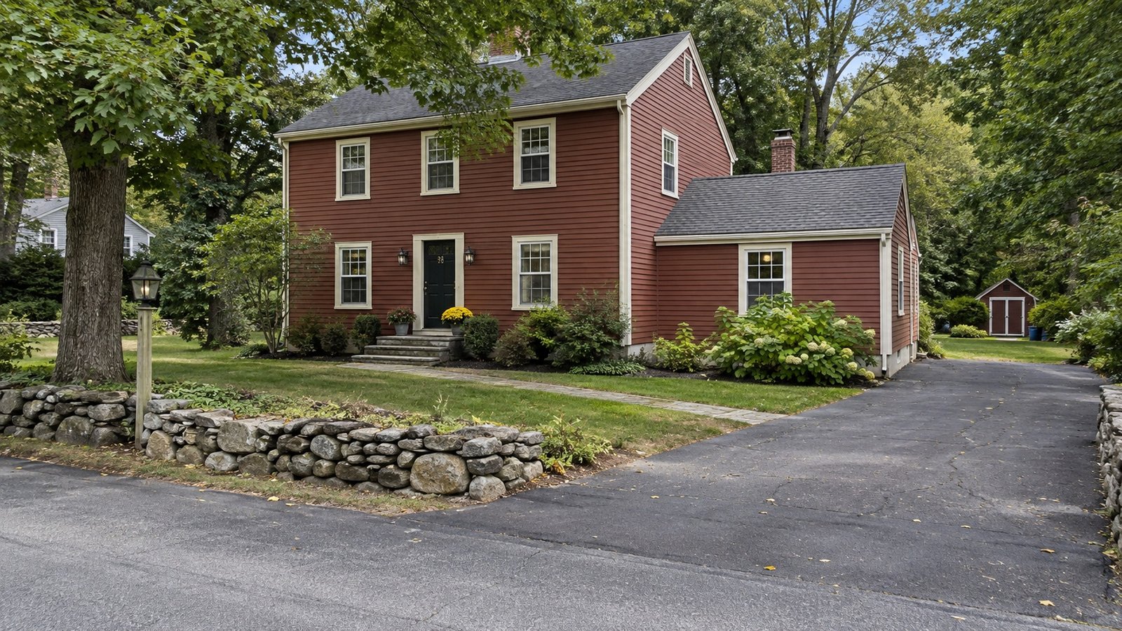 Planning a Groton home move A red-brown clapboard house with cream trim, a paved driveway and a low fieldstone wall