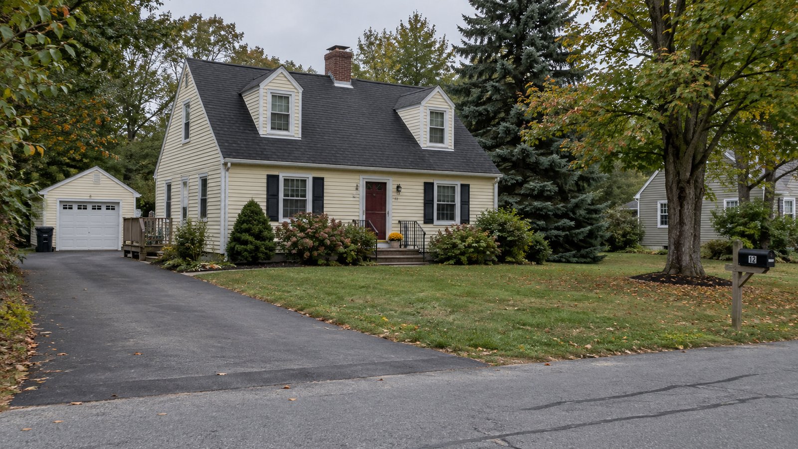 Planning a Hampden residential move A pale-yellow house with dormers, a detached garage and a paved driveway among trees