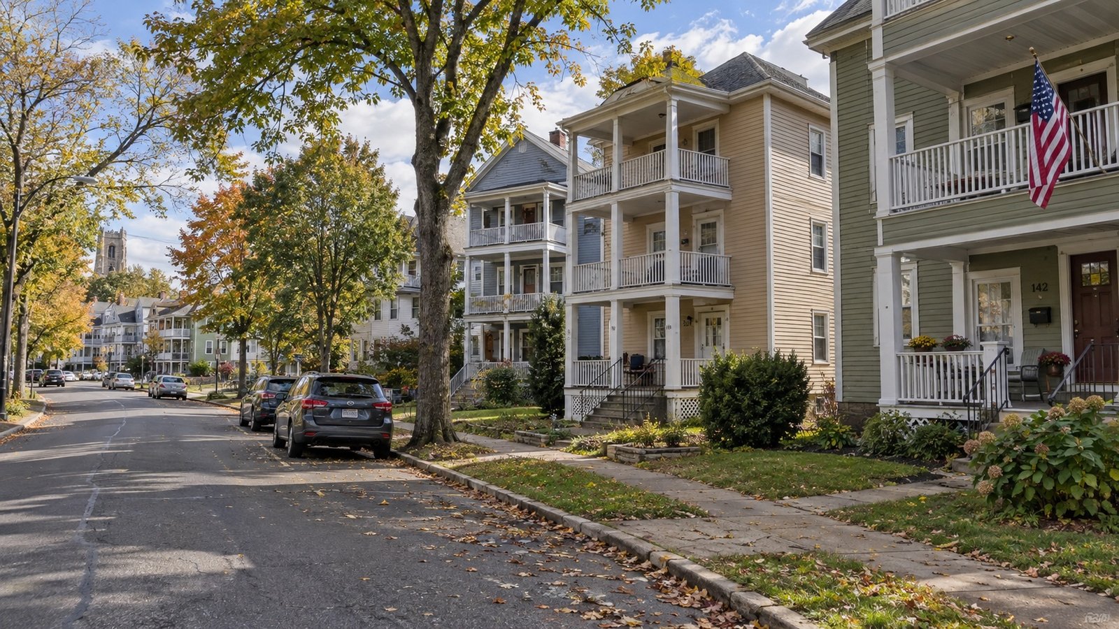 A residential street of wood-frame triple-decker homes with stacked porches and parked cars.