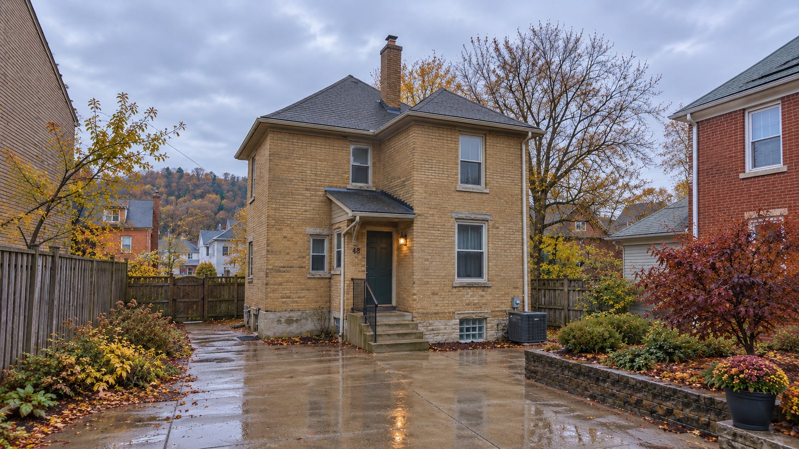 A whole buff-brick house with a sheltered entry and damp courtyard path after a light autumn rain.