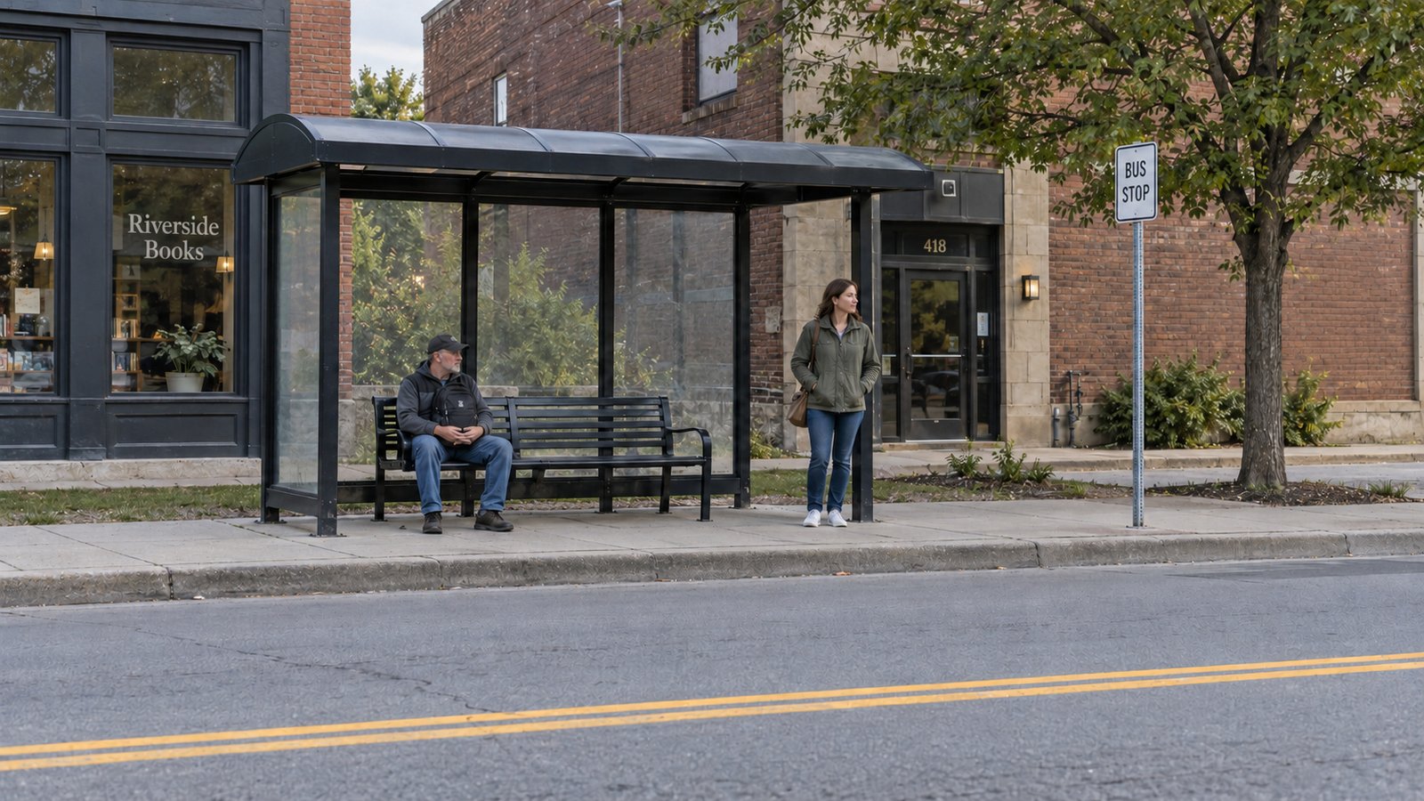 Two adults waiting beside a full bus shelter, bench and functional stop sign along a continuous street.