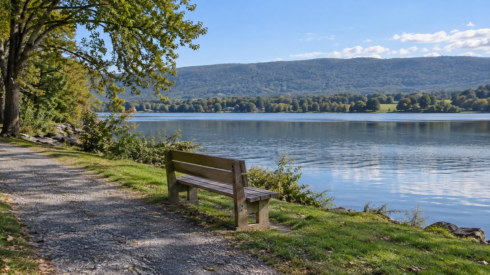 A walk beside the water Wooden bench beside a gravel lakeside path with calm water and a low wooded ridge