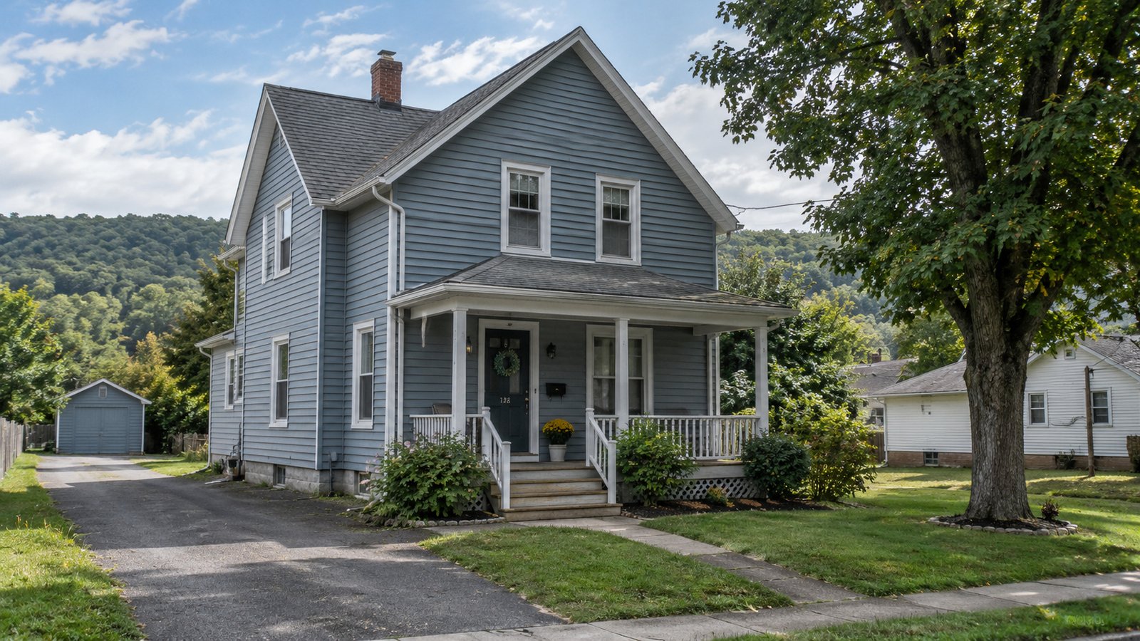 A home in the Bald Eagle Valley Blue-gray two-story home with a covered porch, paved drive and separate garage below a wooded ridge