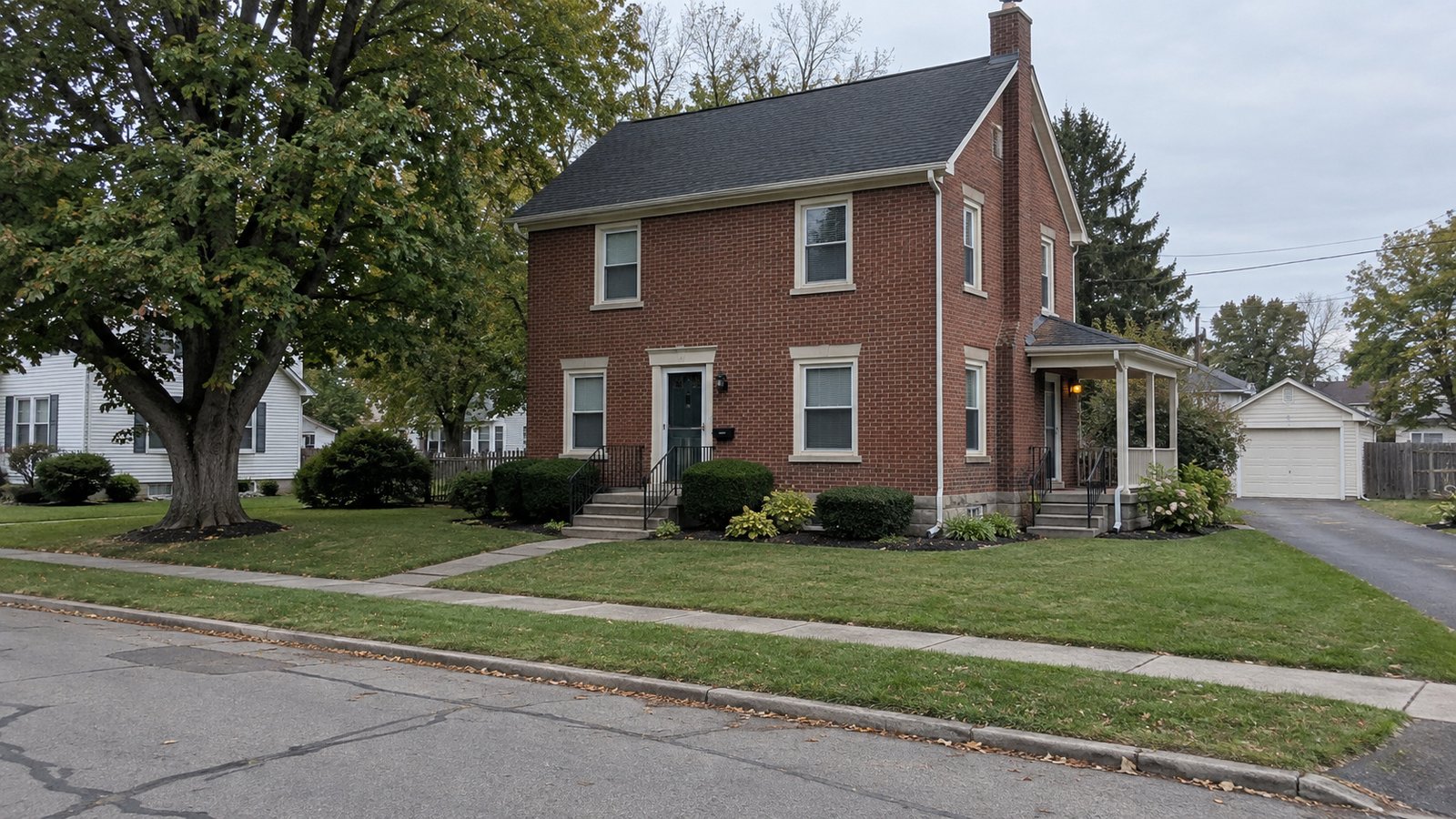 The house and its approach A two-story red brick house with front steps, a side porch, a paved walk and a detached garage.