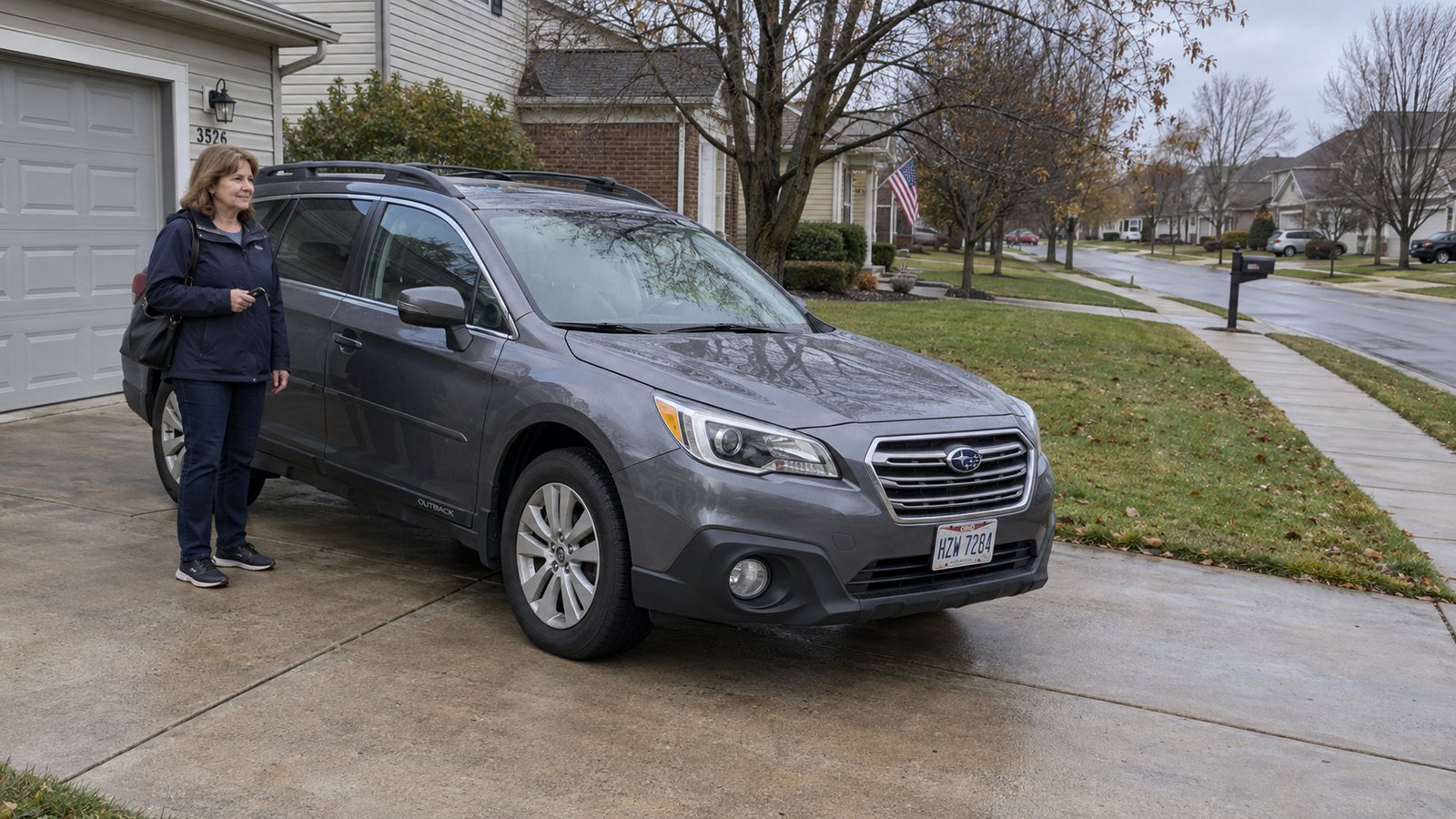 A woman holding keys beside a complete parked gray station wagon on a residential driveway.