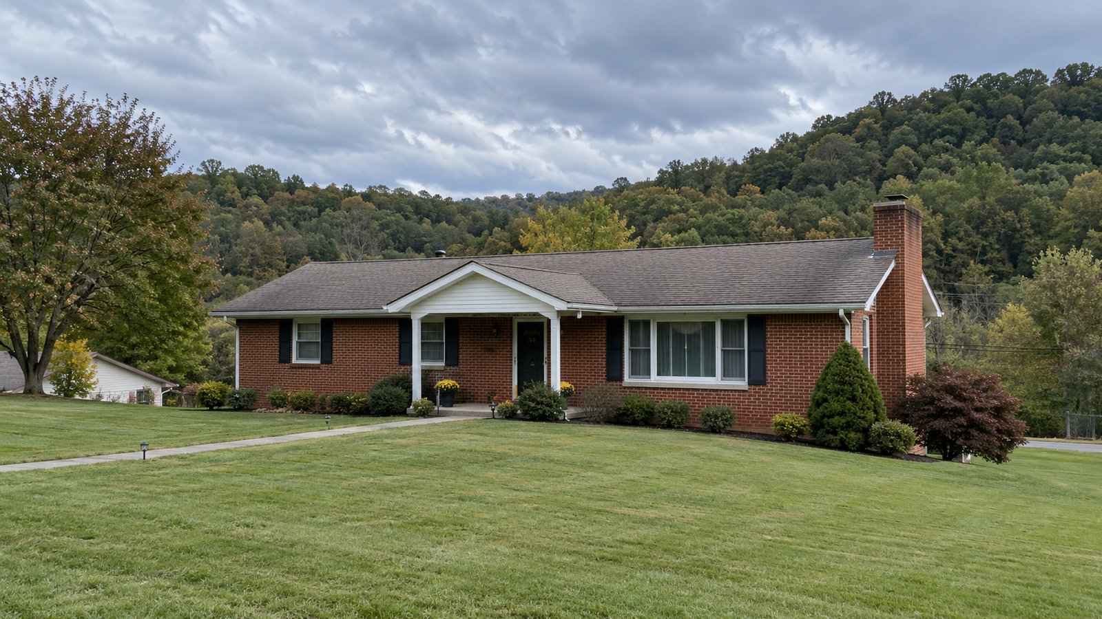 Plan the whole property route A whole modest red brick ranch home with a pitched roof and wooded hills behind.