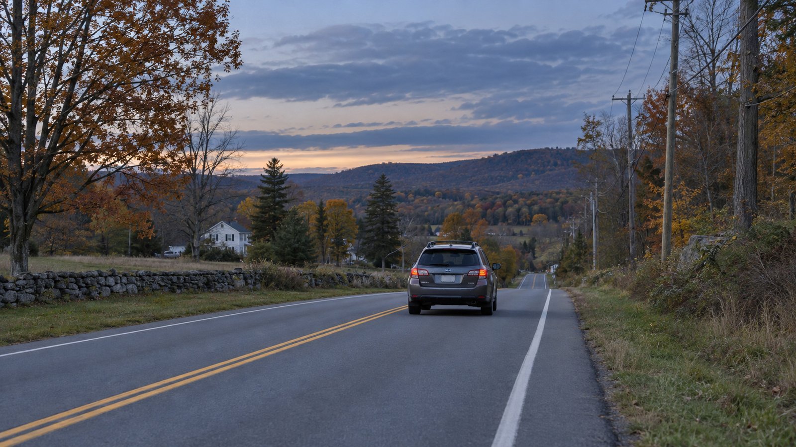 A whole gray wagon travels away in the right lane on a wooded country road.