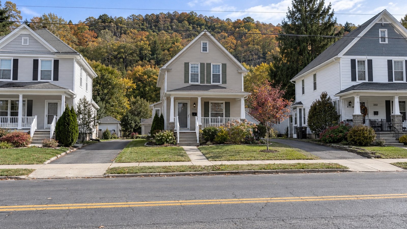The property approach Three older houses with front porches, joined paths and driveways beside a quiet two-way road and wooded ridge.