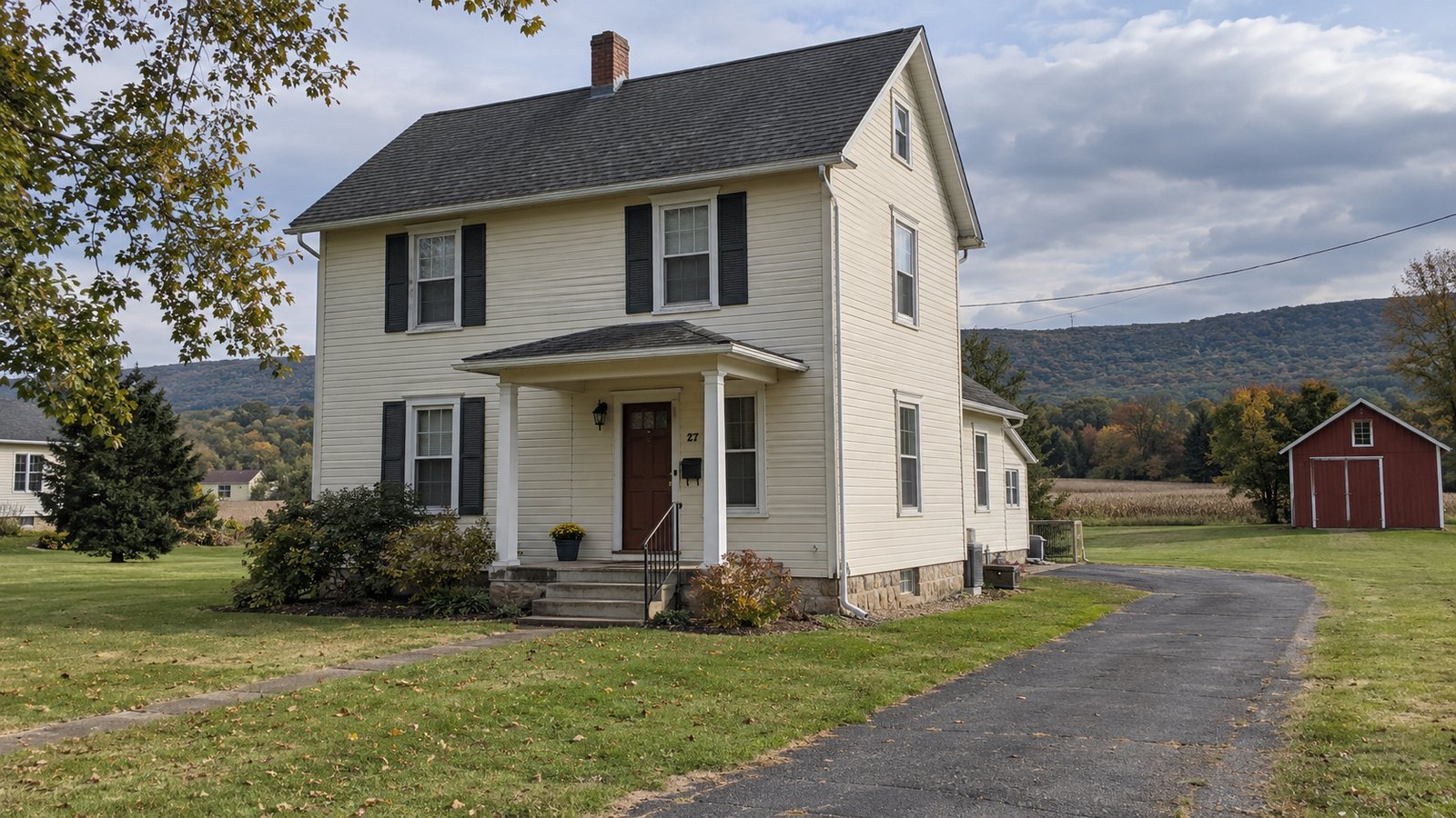 A house in a Pennsylvania valley A cream two-story house with a covered entrance, paved driveway and red outbuilding