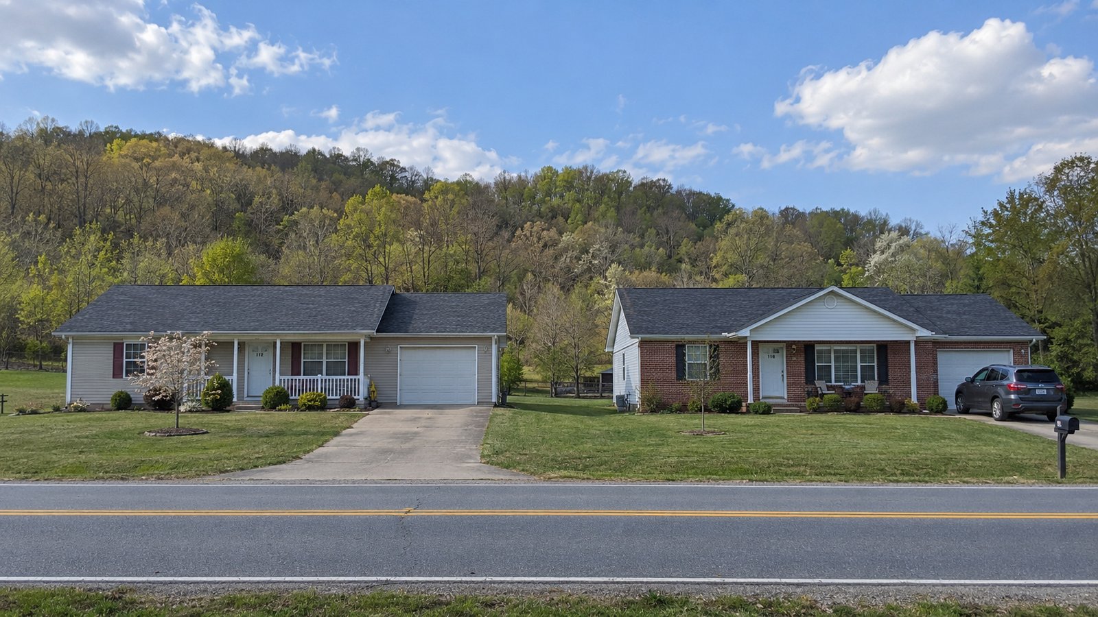 Read the outside approach Two complete one-story houses and driveways beside a straight road and wooded ridge.