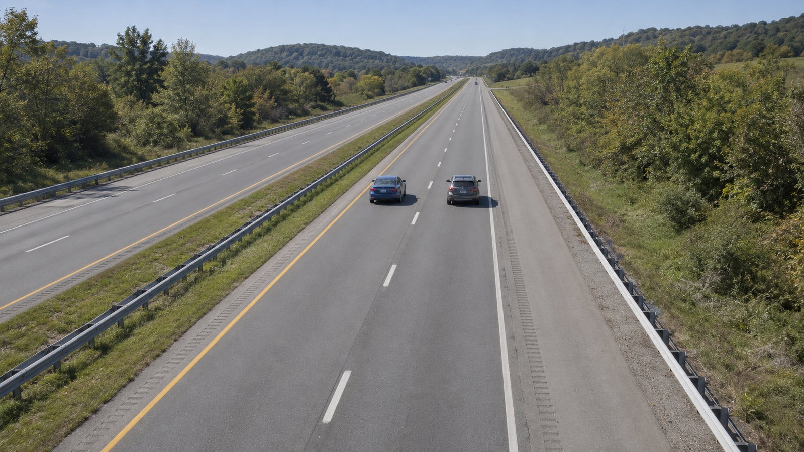 Test the ordinary journey An elevated view of two small cars on separate lanes of a straight divided highway beside wooded hills.