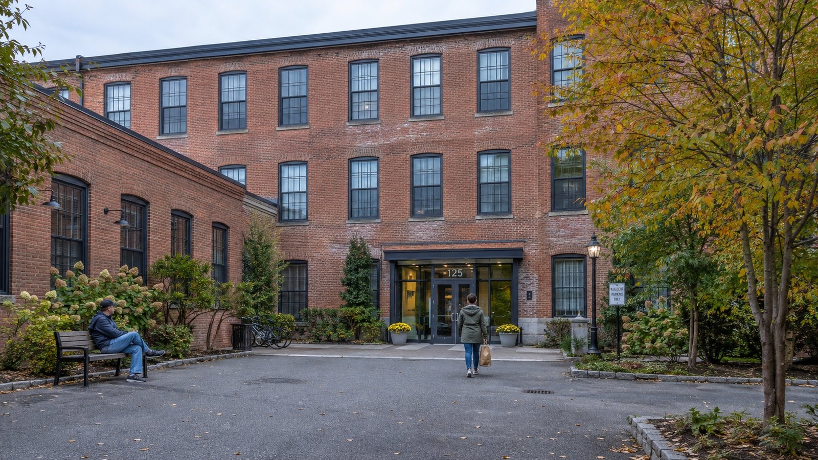 Brick apartment building around a paved courtyard, with a resident arriving and another sitting on a bench.