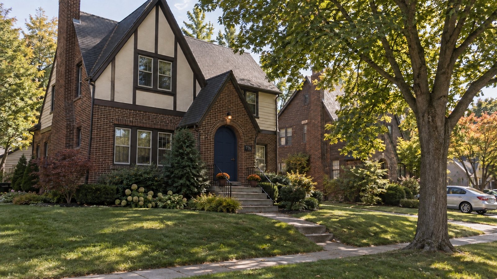 Brick and cream stucco house with an arched entrance beneath a mature maple tree