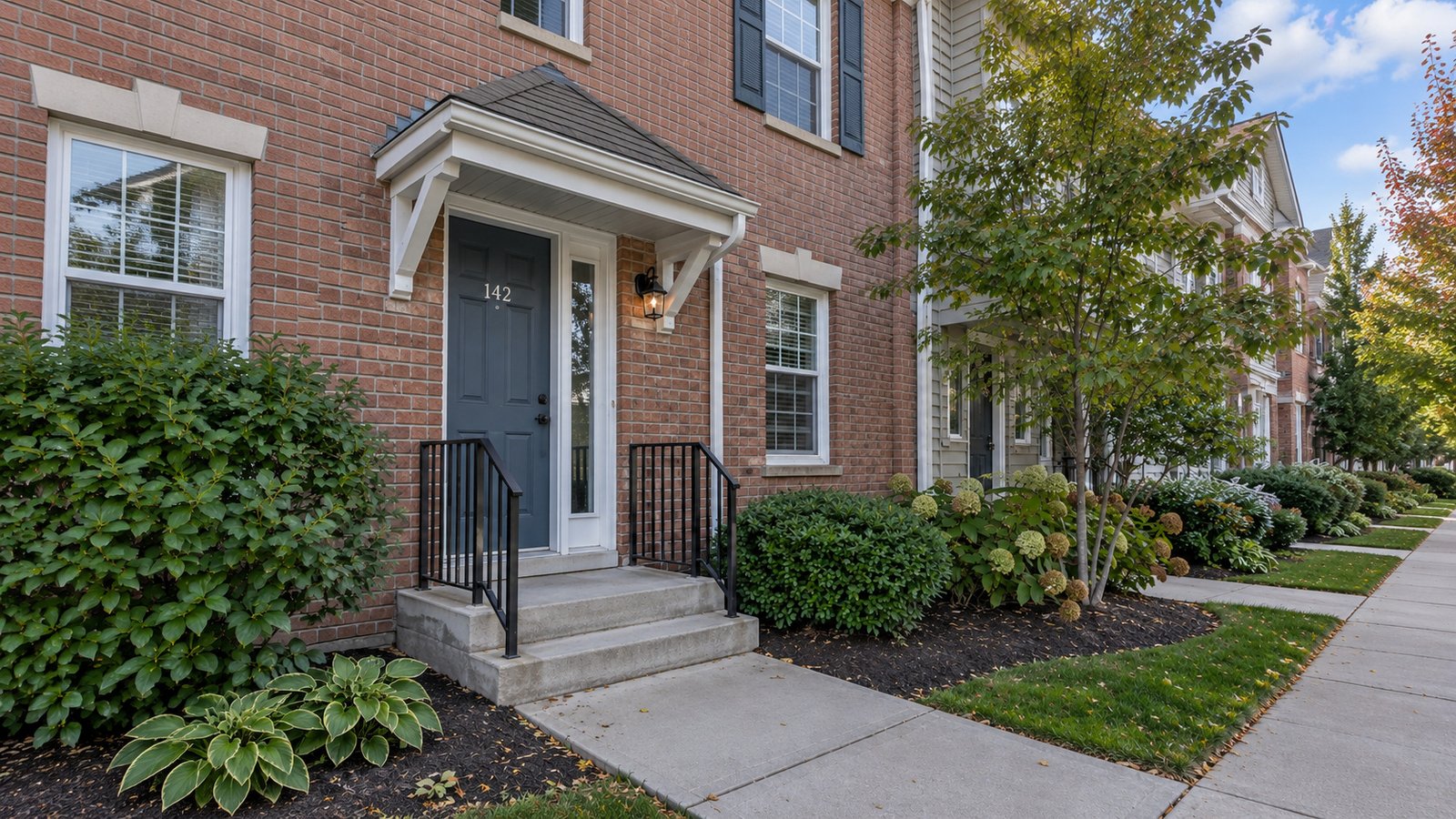 Show the entrance and landing A brick townhouse entrance with a closed dark door, sidelights, covered landing and two concrete steps.