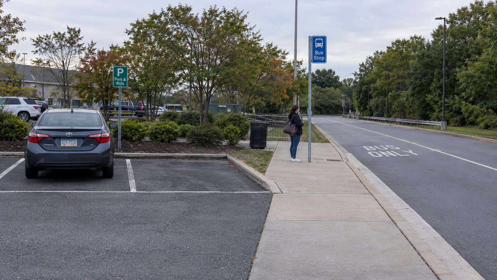 A woman waiting at a bus-stop pole beside a marked bus lane, with a car in a separate parking bay.