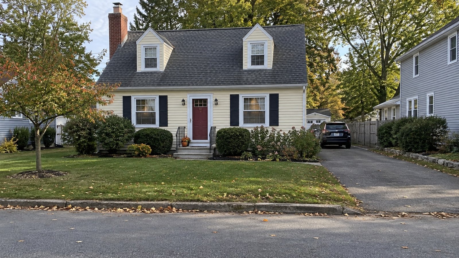 A Cape house and its approach Pale yellow Cape house with two dormers, brick chimney, front steps and a paved side driveway